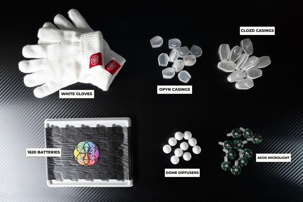 Beginner glove set laid out flat, showing gloves, OPYN and CLOZD casings, batteries, dome diffusers, and the AEOS microlight as separate labeled pieces
