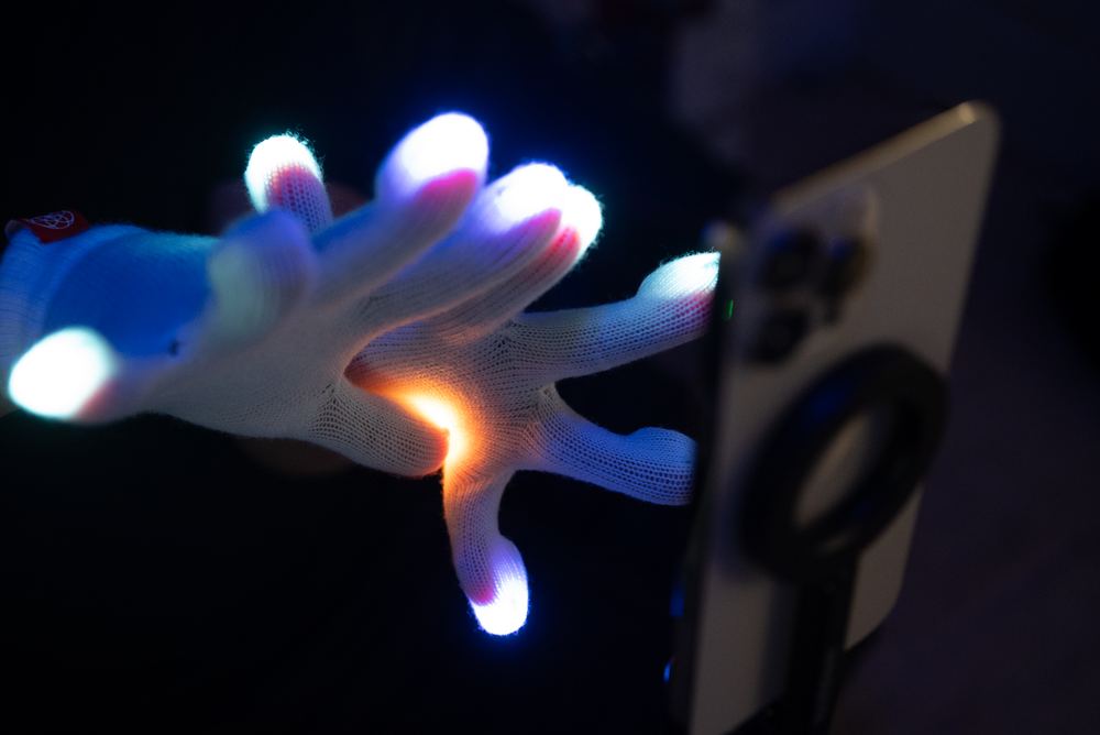 A gloved hand reaching toward a phone propped up to film a practice session at home