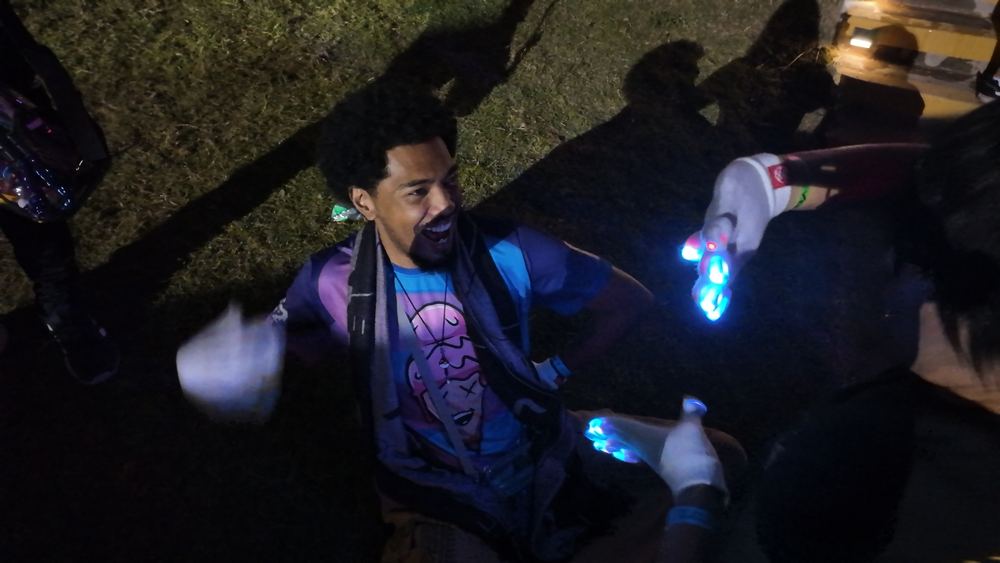 Two glovers trading a lightshow candidly at an outdoor festival meetup