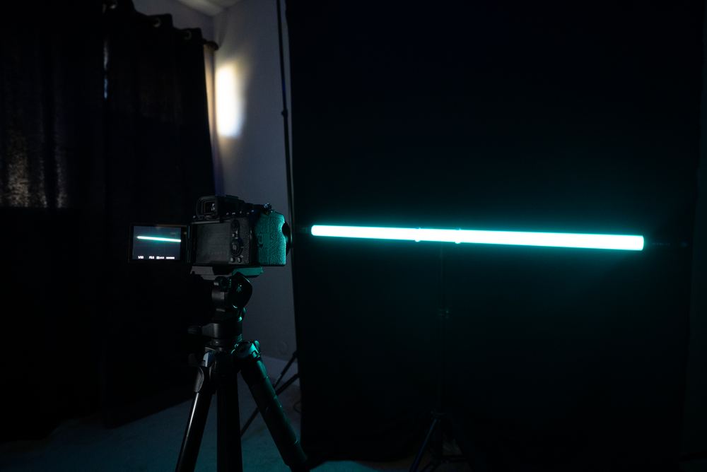 Behind-the-scenes of an actual filming setup: dark backdrop, camera on a tripod, subtle teal accent lighting