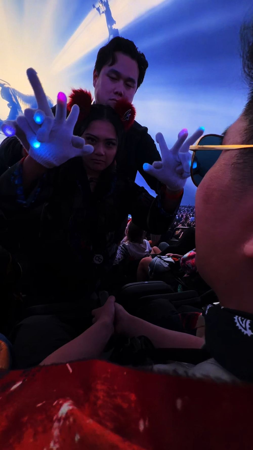 Two glovers reaching toward the viewer together in sync, both wearing lit gloves at a festival
