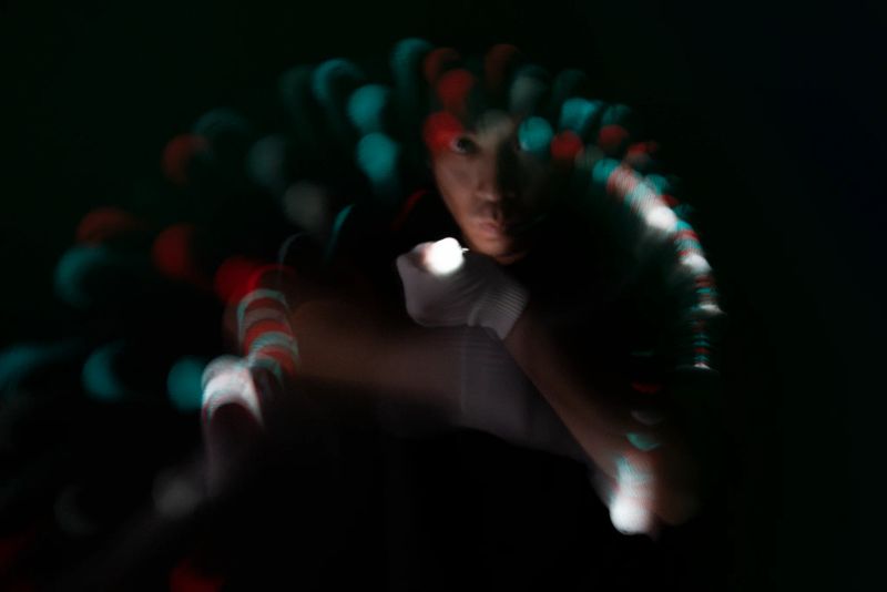 Glover mid-move with a glowing light trail circling their lit hand, face softly visible in shadow