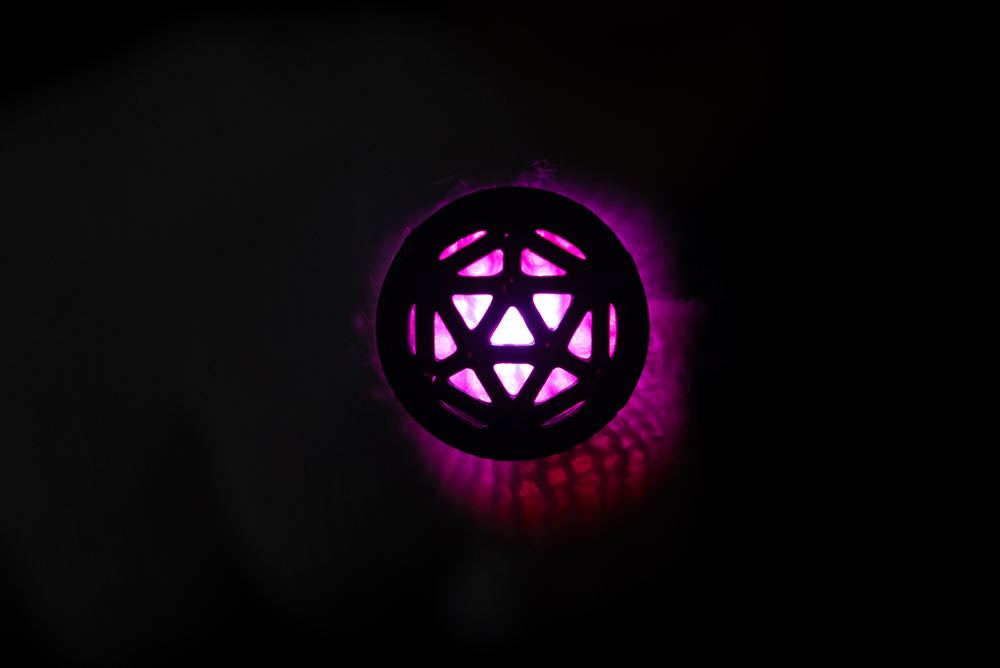 A diffuser cap installed on a microlight, lit up in a dark room showing a geometric cut-out pattern