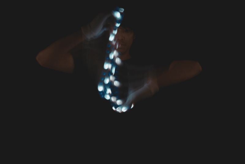 Glover reaching toward the camera with a vertical chain of glowing LED beads trailing from lit fingertips